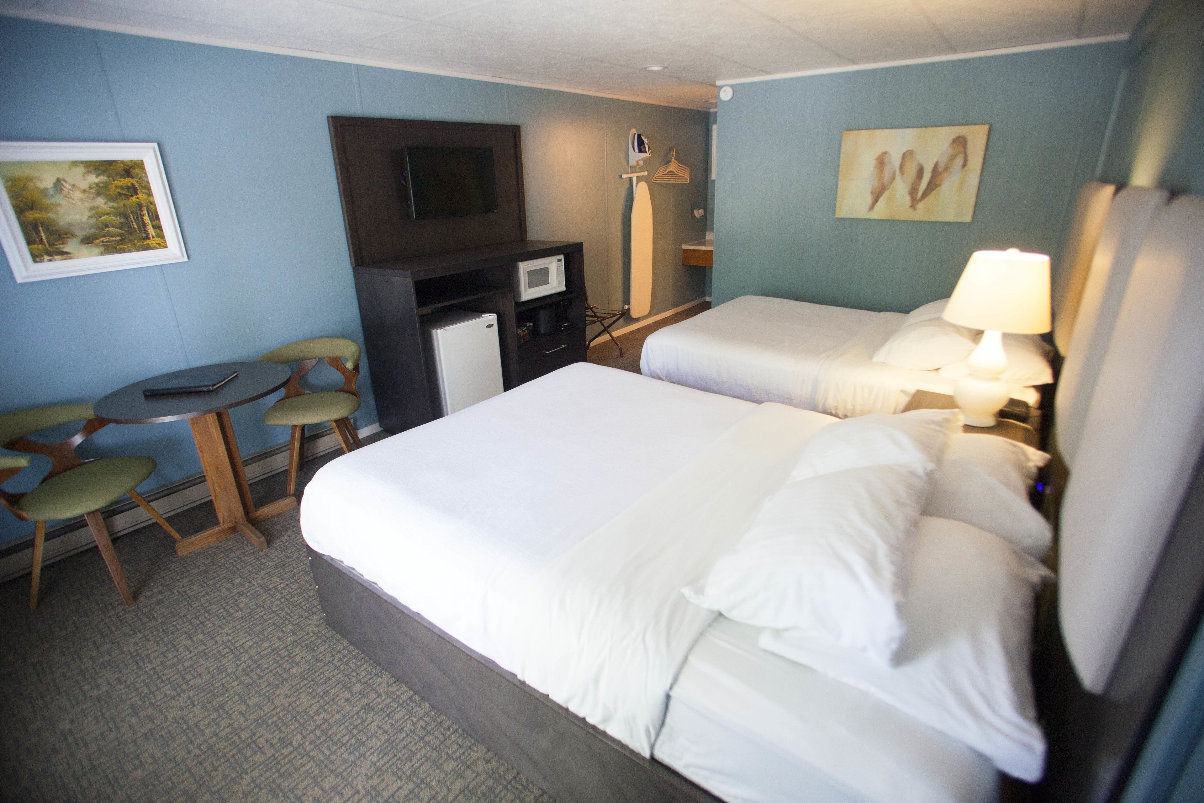 A hotel room with two beds, a desk, a chair, a TV, and a microwave.