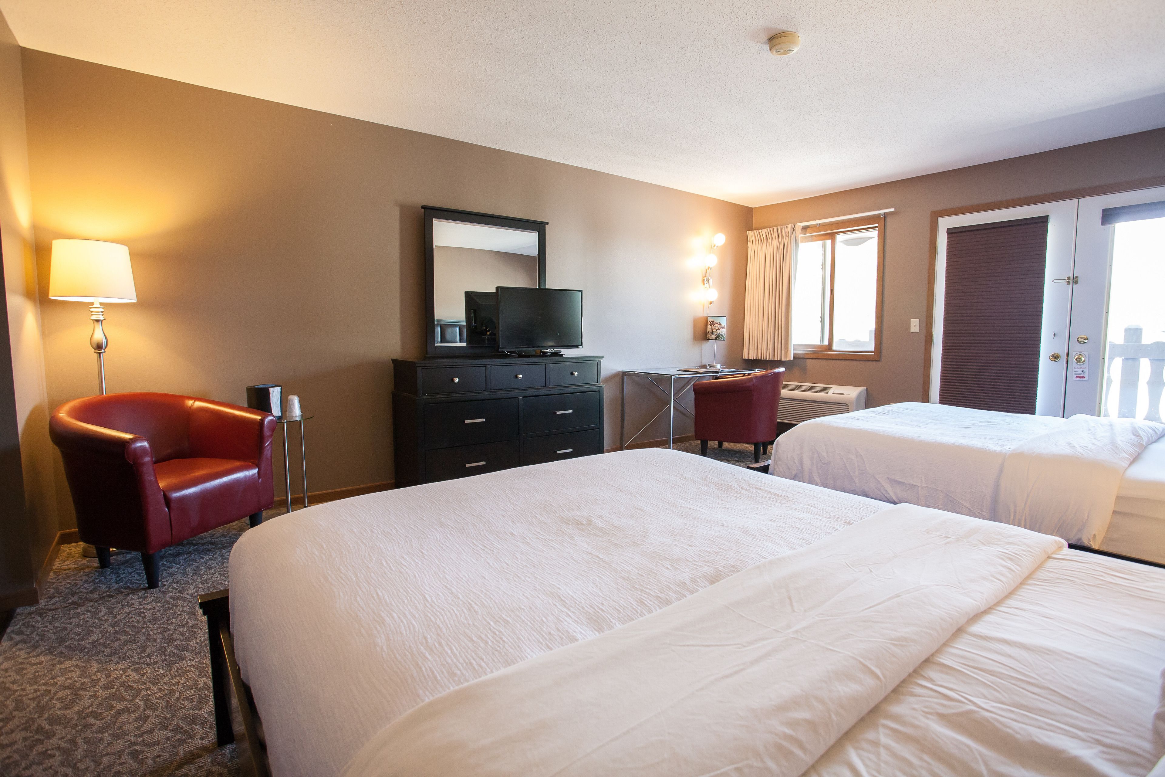 Une chambre d’hôtel avec deux lits, un bureau, une chaise, une télévision et une lampe.