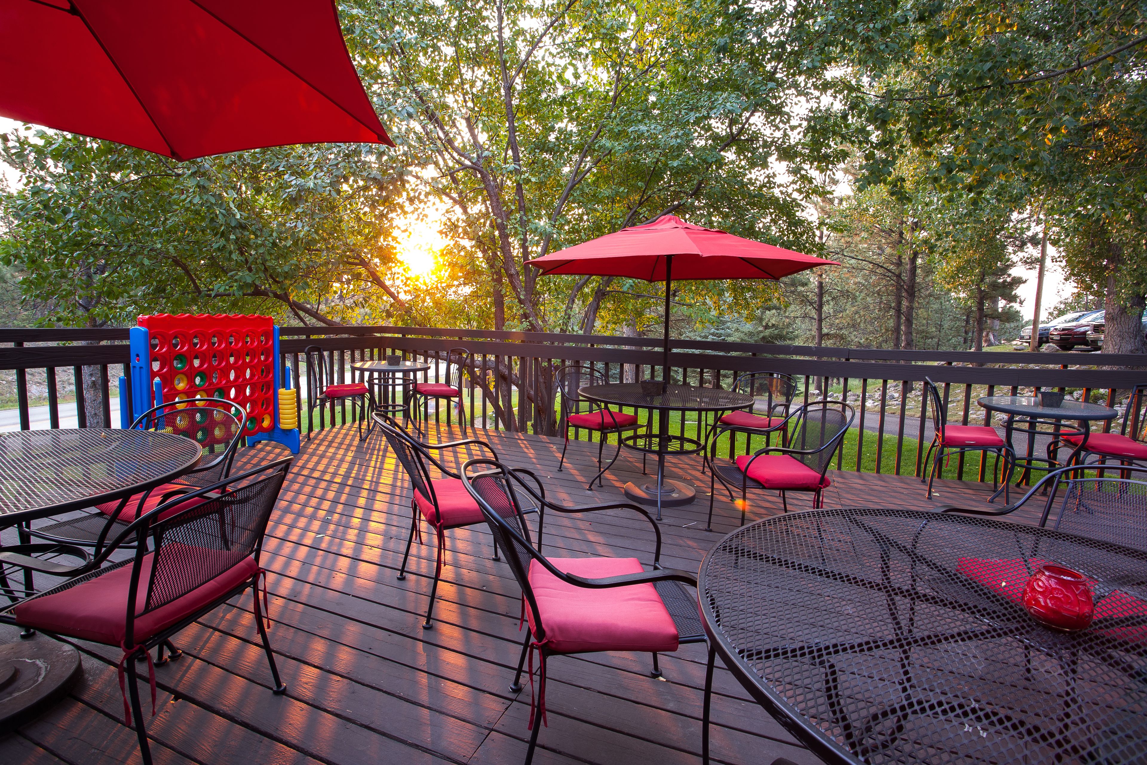 Eine Terrasse im Freien mit Metalltischen und -stühlen, roten Kissen und Sonnenschirmen.
