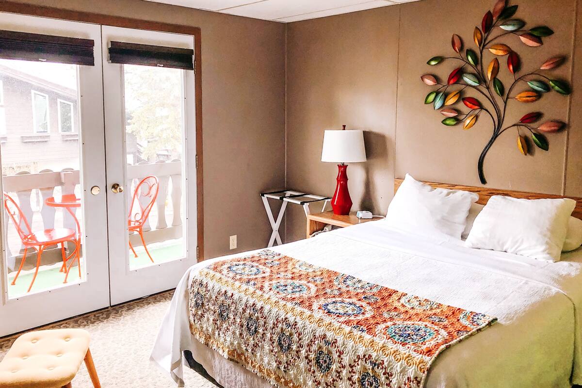 Habitación de hotel con cama, mesita de noche, lámpara, silla y vista al exterior por una puerta corrediza.