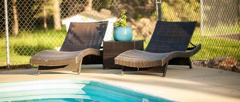 A poolside area with two wicker lounge chairs and a potted plant.