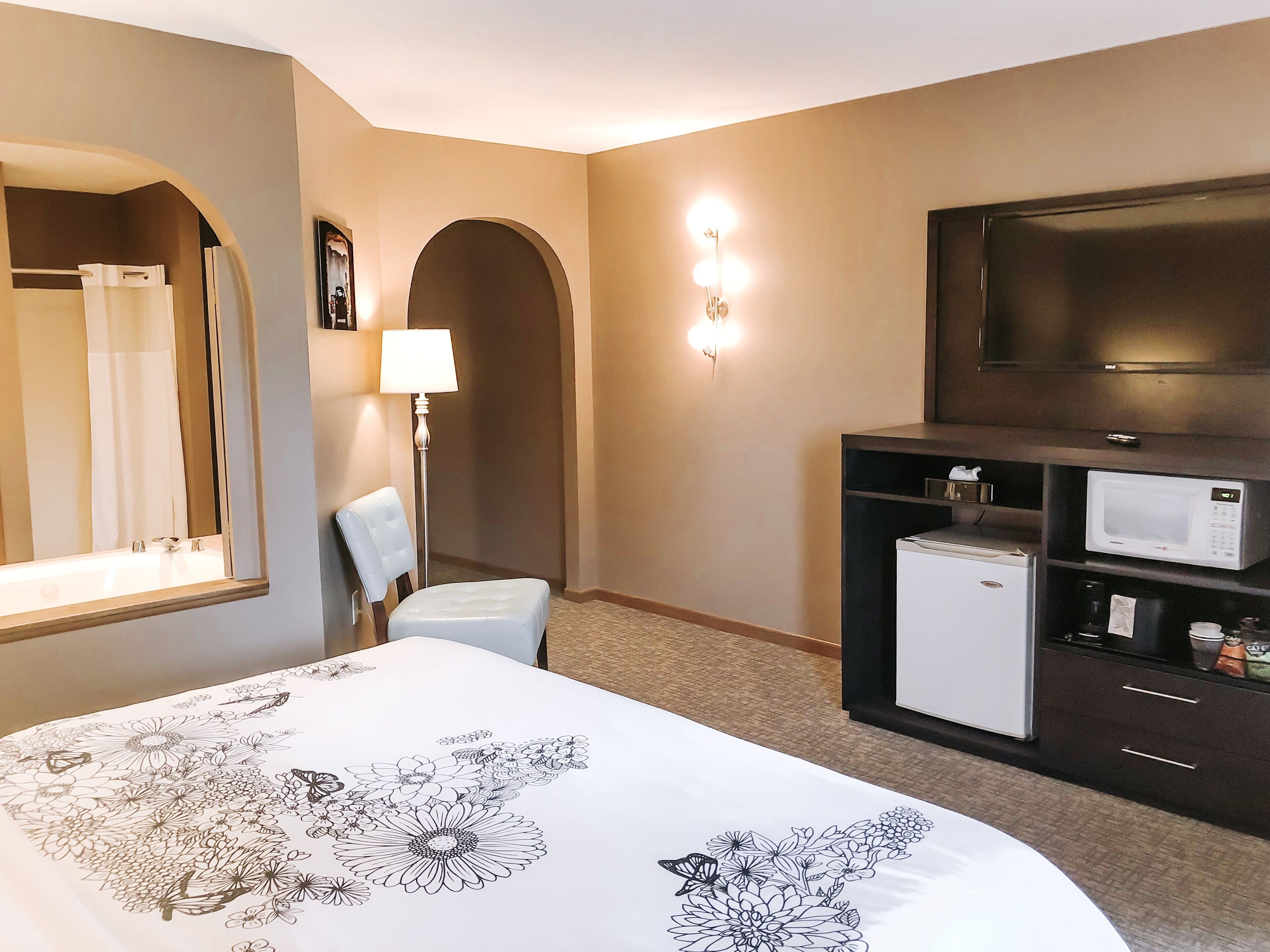 A hotel room with a bed, a TV, a refrigerator, a microwave, a lamp, and a mirror.