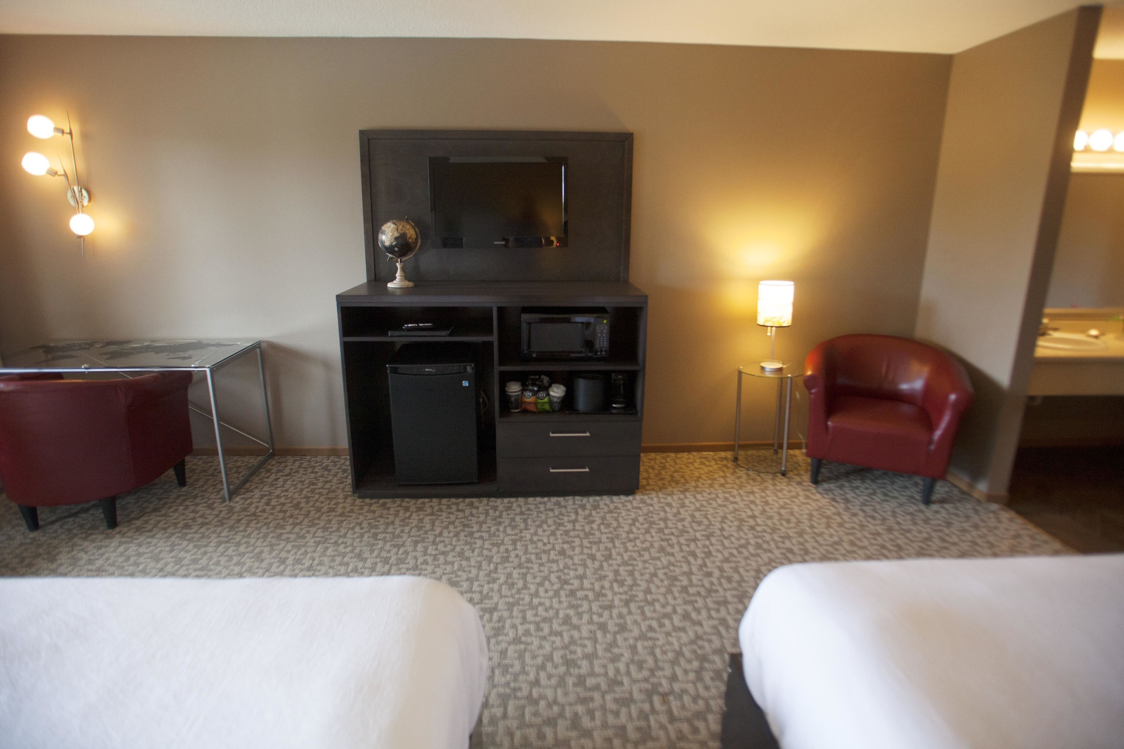 Ein Hotelzimmer mit Schreibtisch, zwei roten Sesseln, einer Minibar, einem Fernseher und einer Lampe.