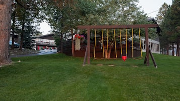 Relax in a serene setting with a charming wooden swing set amidst lush greenery and a distant house.