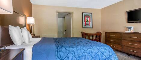 A hotel room with a bed, a desk, a chair, a dresser, and a television.
