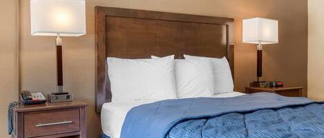 Una habitación de hotel con una cama, dos mesitas de noche, una lámpara y un teléfono.
