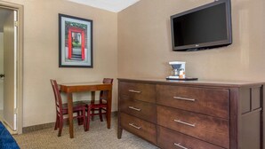 Ein Hotelzimmer mit Holztisch, Stühlen, einem Schminktisch, einem Flachbildfernseher und einem gerahmten Bild an der Wand.