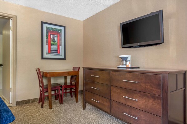 Habitación de hotel con escritorio de madera, sillas, cómoda, televisor de pantalla plana y un cuadro en la pared.