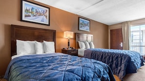 Ein Hotelzimmer mit zwei Betten, einem Nachttisch, einer Lampe und gerahmten Bildern an der Wand.