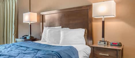 A hotel room with a large bed, two bedside lamps, a nightstand with a clock, and a wooden headboard.