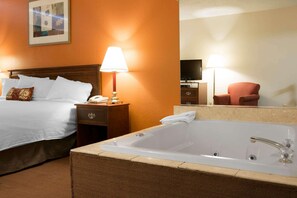 Habitación de hotel con una cama grande, una zona de estar con una silla, una bañera y un televisor.