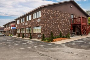 A motel with a brick facade, a covered outdoor seating area, and a parking lot.