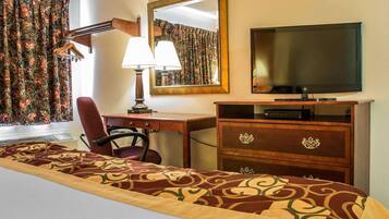 Quarto de hotel com cama, escrivaninha com cadeira, televisão, cómoda e espelho.