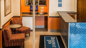 Eine Hotelhalle mit gestreiften Sesseln, einem Empfangstresen, einer Wand aus blauen Ziegeln und einer Fußmatte mit der Aufschrift "RODEWAY INN".