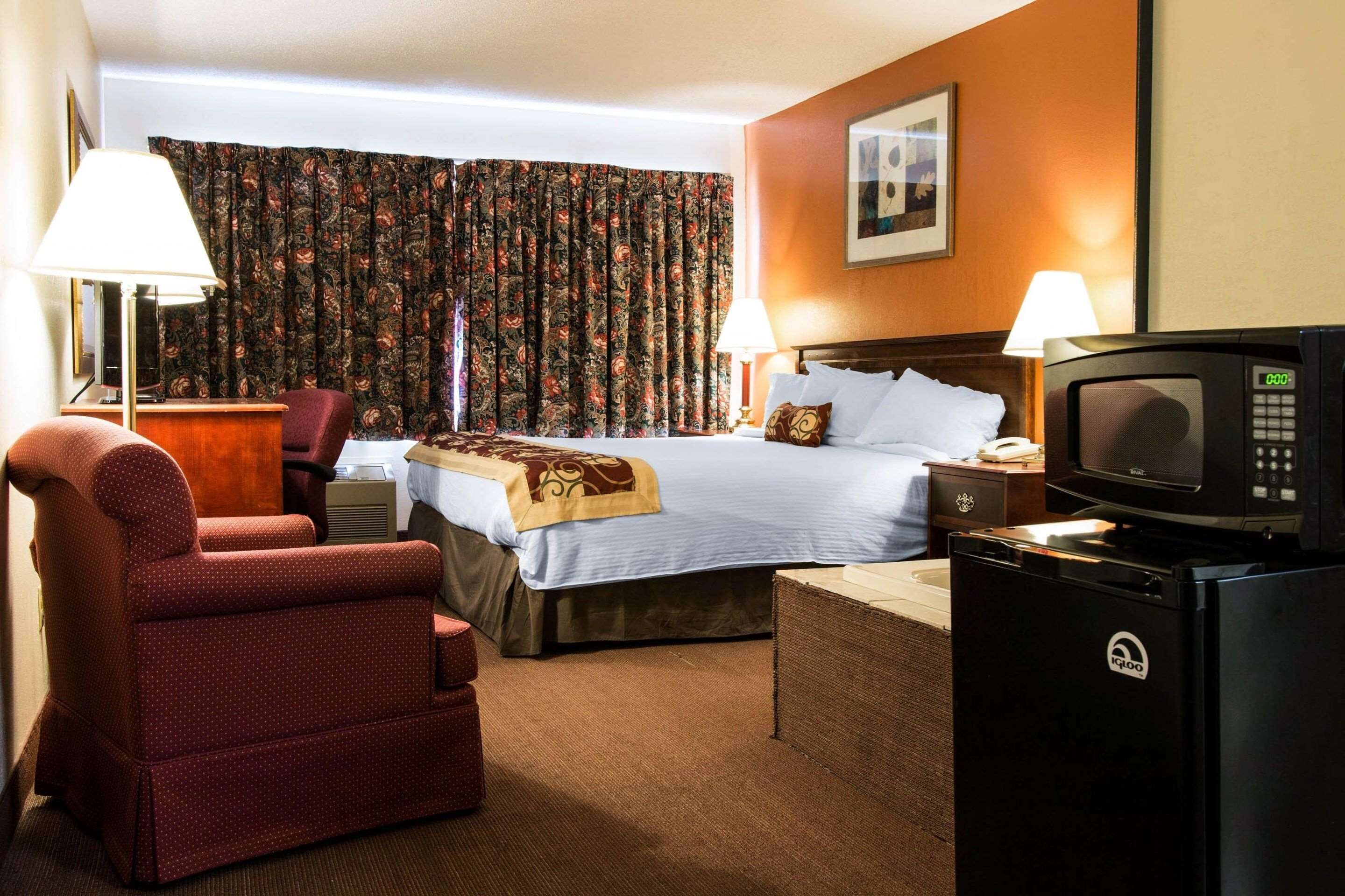 Una habitación de hotel con una cama, un sillón rojo, un escritorio con lámpara, un microondas y una televisión.