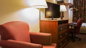 Ein Hotelzimmer mit einem roten Ledersessel, einer Holzkommode mit Fernseher und einem Schreibtisch mit Lampe.