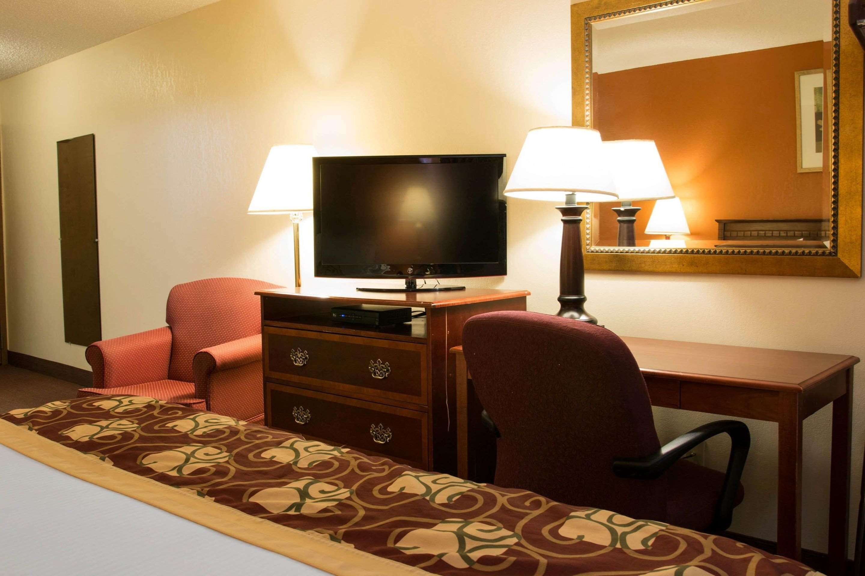 A hotel room with a bed, a desk with a television, two lamps, a chair, and a dresser.