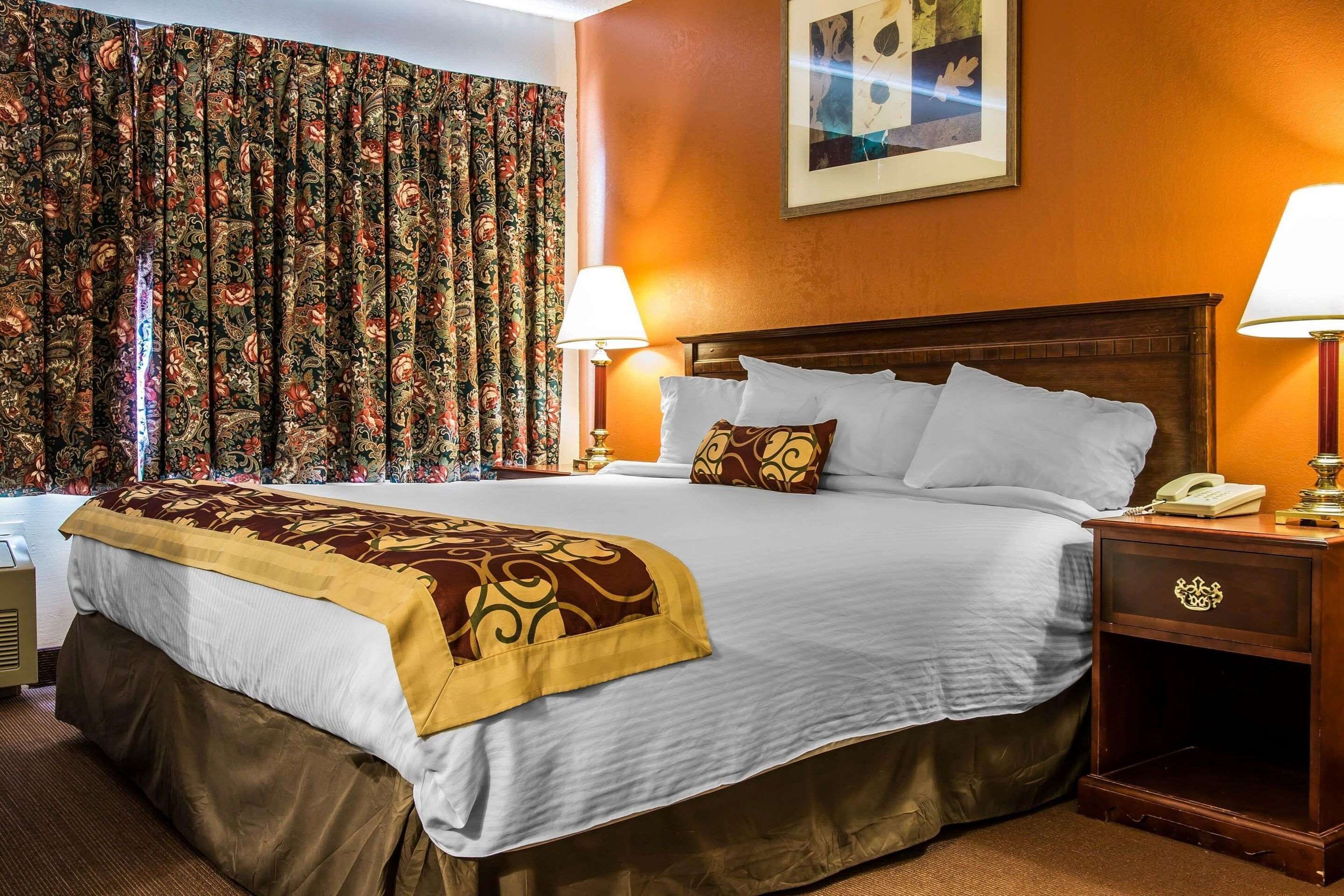 A hotel room with a large bed, two bedside lamps, a nightstand with a phone, and a floral curtain.