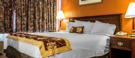 A hotel room with a large bed, two bedside lamps, a nightstand with a phone, and a floral curtain.