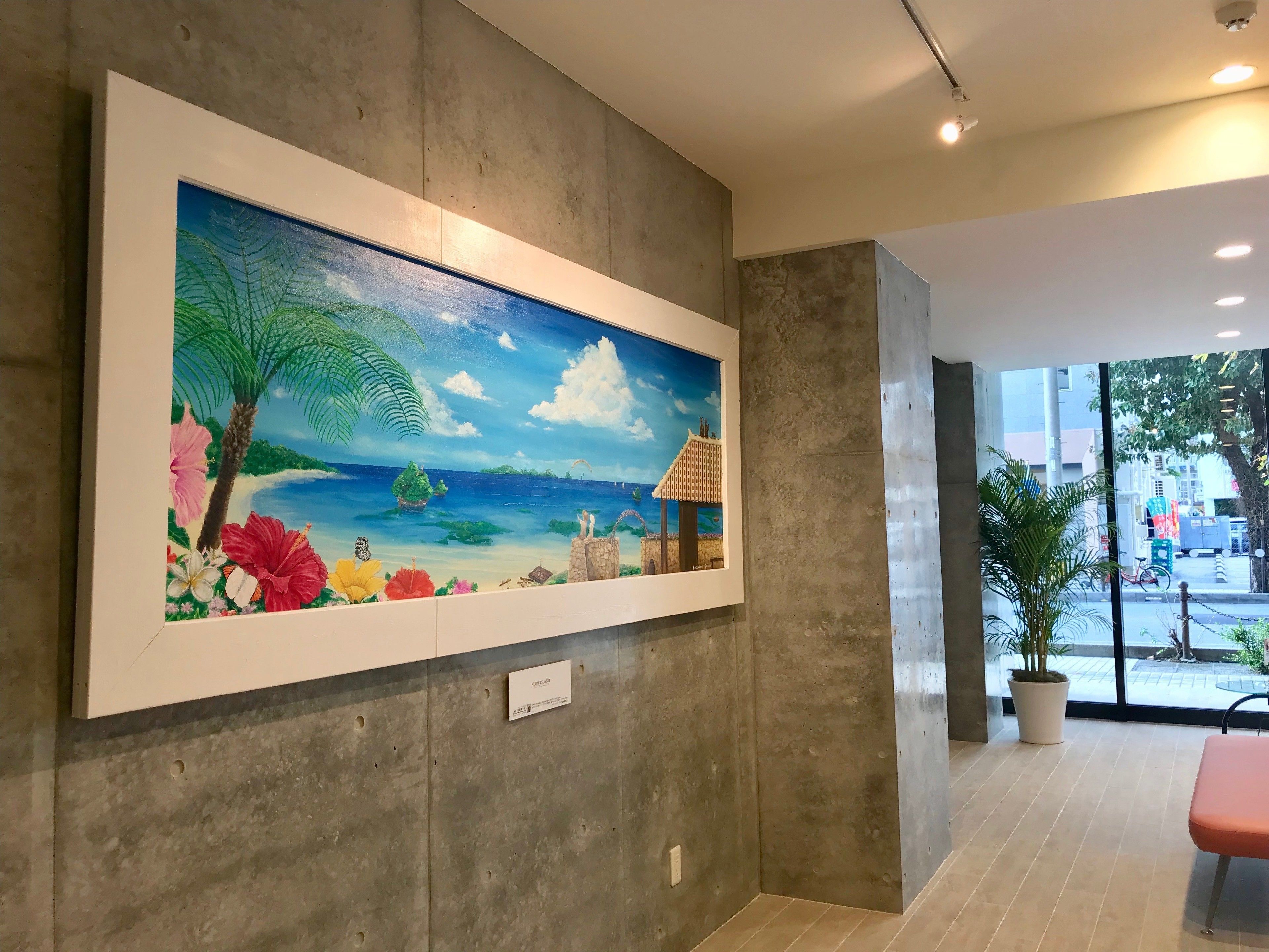 Un grand tableau encadré représentant une scène de plage tropicale, accroché au mur du hall d’un hôtel.