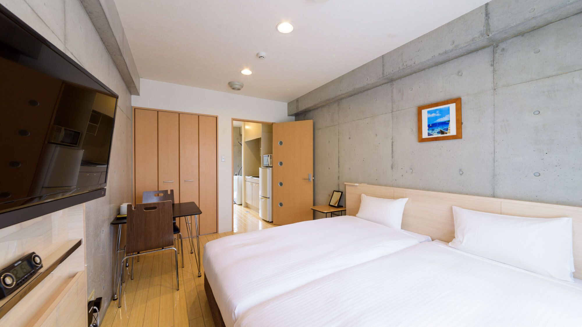 Una habitación de hotel con cama, escritorio, silla, televisión y kitchenette.