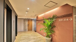 Zona de recepción de hotel con suelo de madera, una planta en maceta y una pared con un número de teléfono y una flecha direccional.