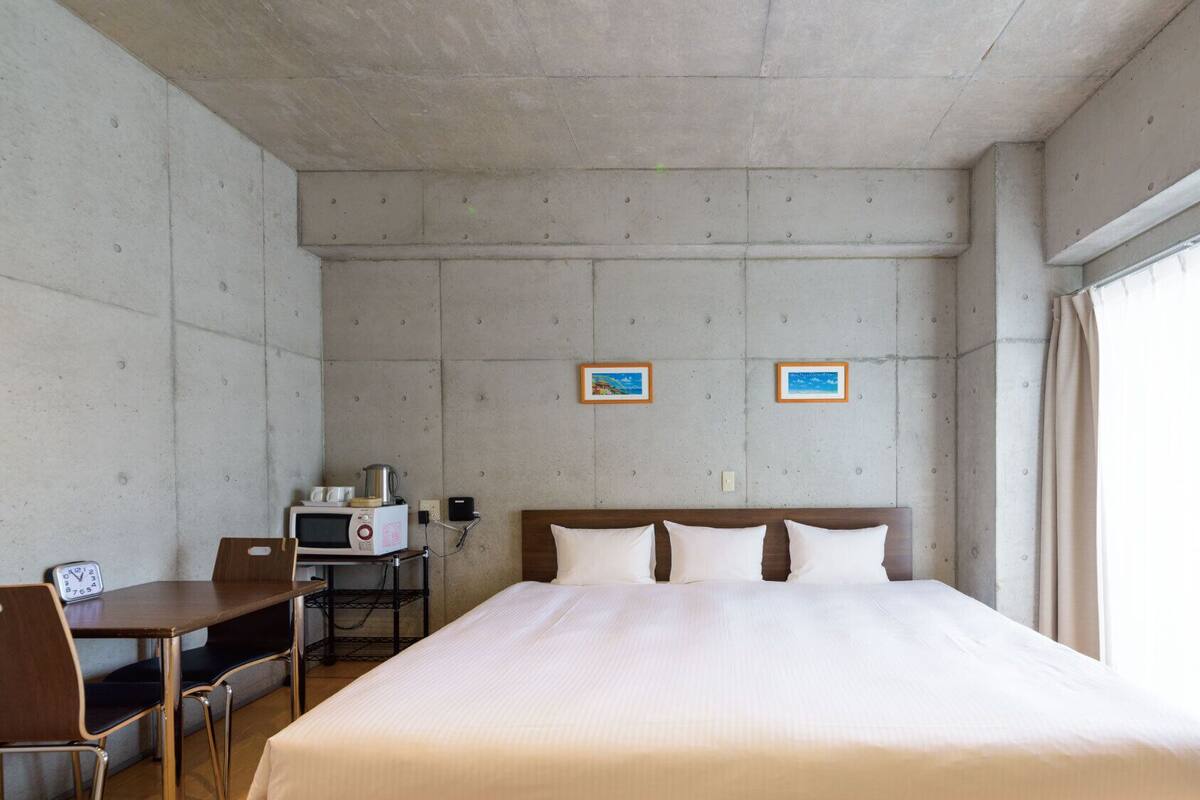 A hotel room with a bed, a desk with a chair, a microwave, and two framed pictures on the wall.