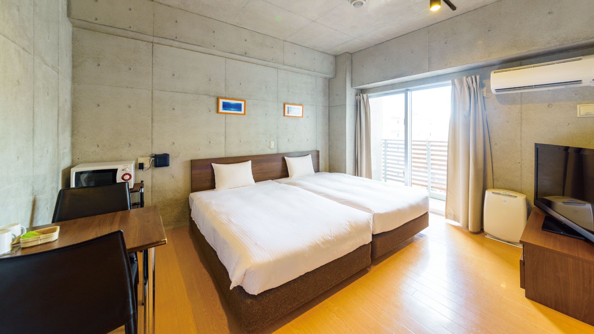 Una habitación de hotel con cama, escritorio, silla, aire acondicionado y televisión.