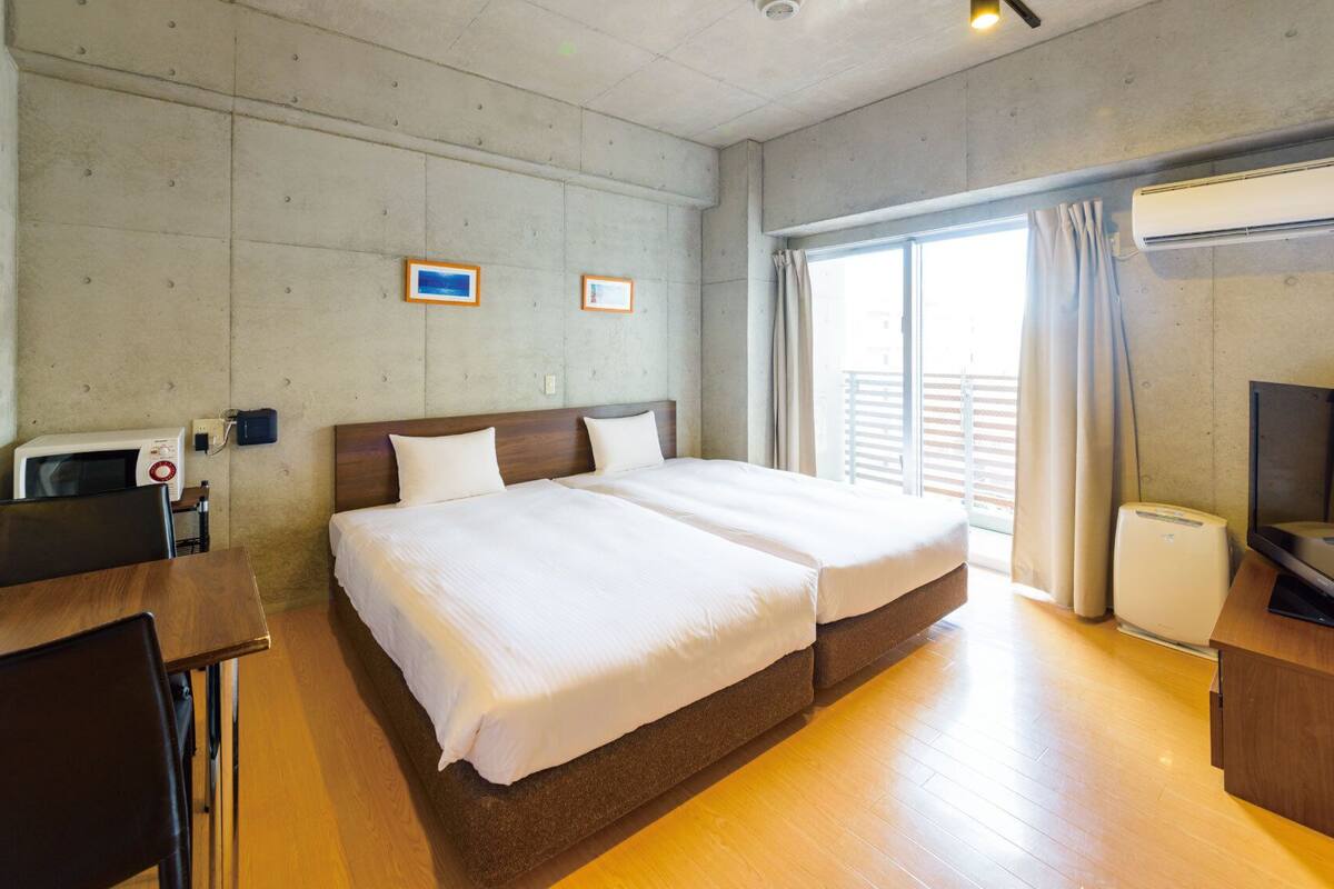 A hotel room with a bed, a desk, a chair, an air conditioner, and a television.