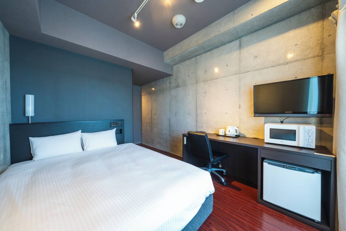 A hotel room with a bed, a desk with a computer, a microwave, and a TV.
