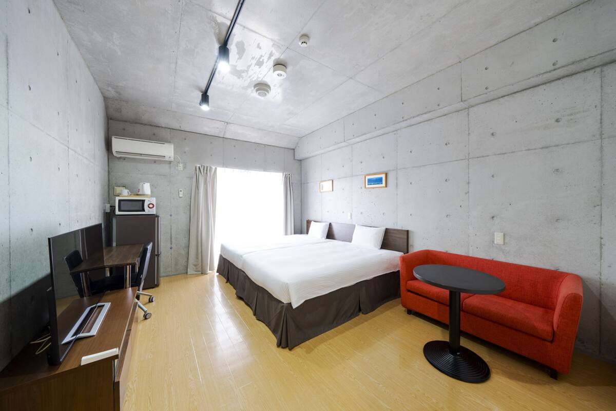 A hotel room with a bed, a desk with a computer, a red sofa, and a small table.