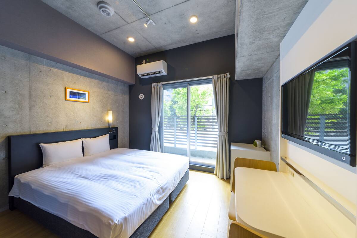 A modern bedroom with a large bed, a desk, and a window with curtains.