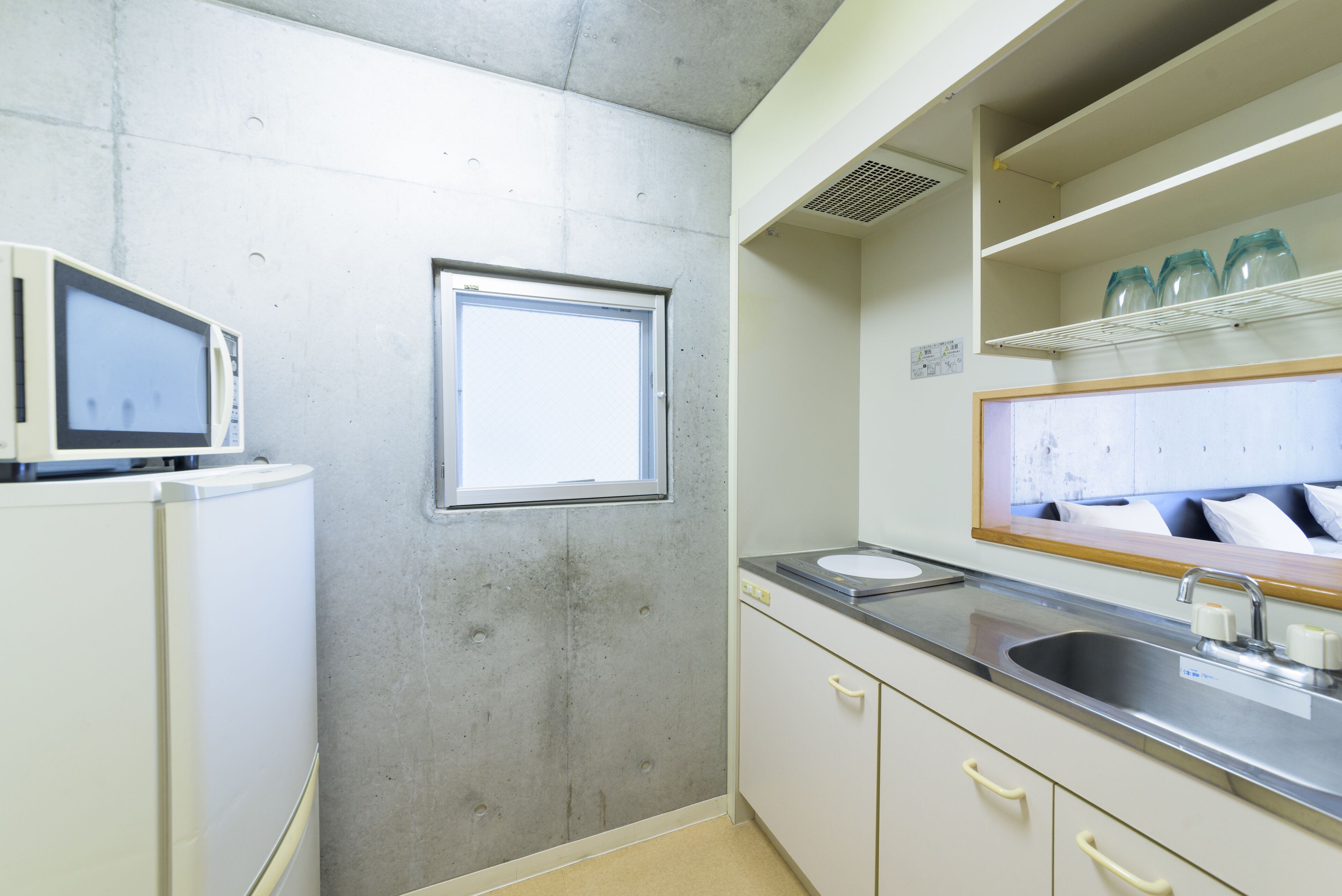 A kitchen with a microwave, a window, a sink, and a shelf with jars.