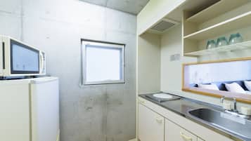 A kitchen with a microwave, a window, a sink, and a shelf with jars.
