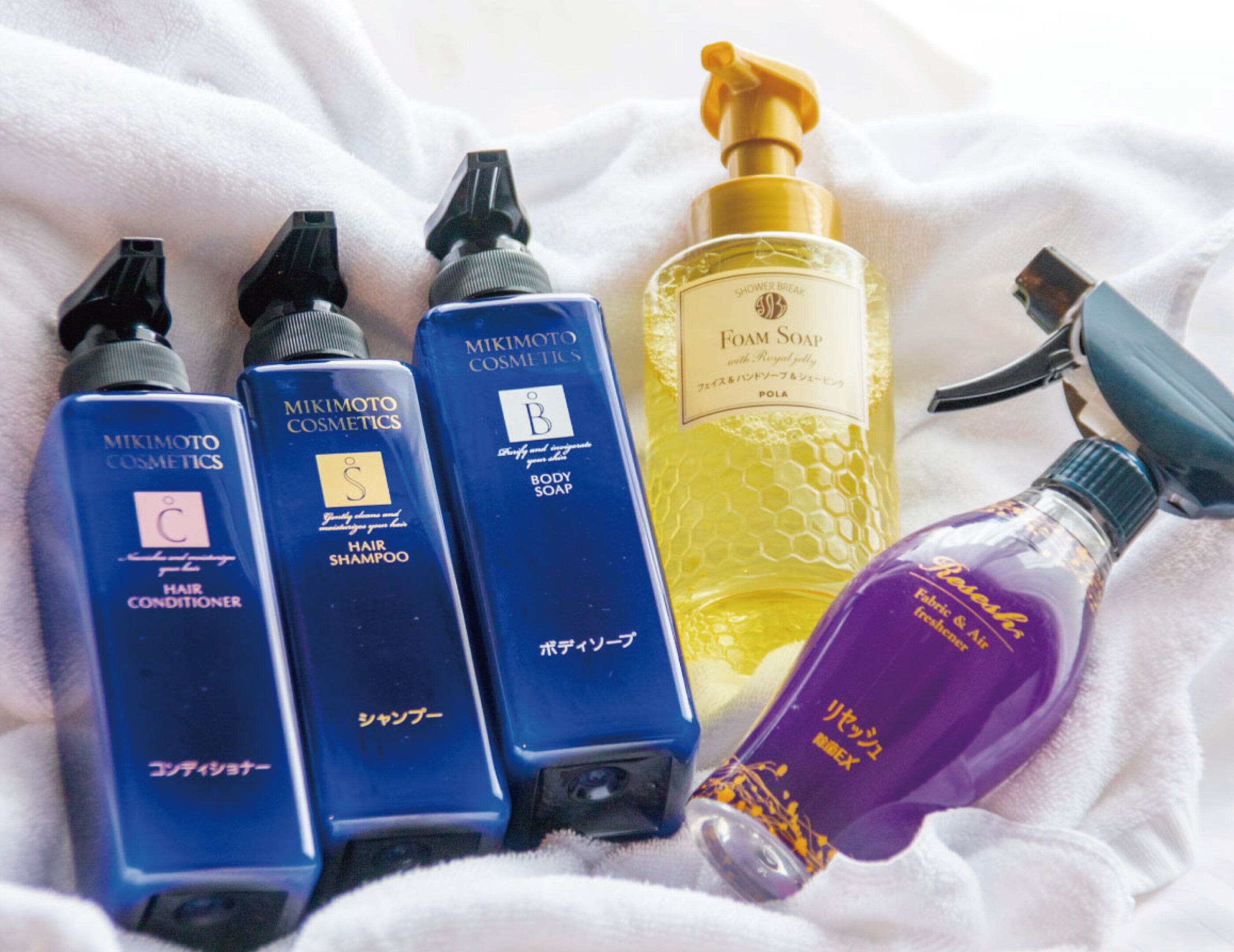 Variedad de productos de cuidado personal, incluyendo acondicionador para el cabello, jabón corporal y un atomizador, sobre una superficie de tela blanca.