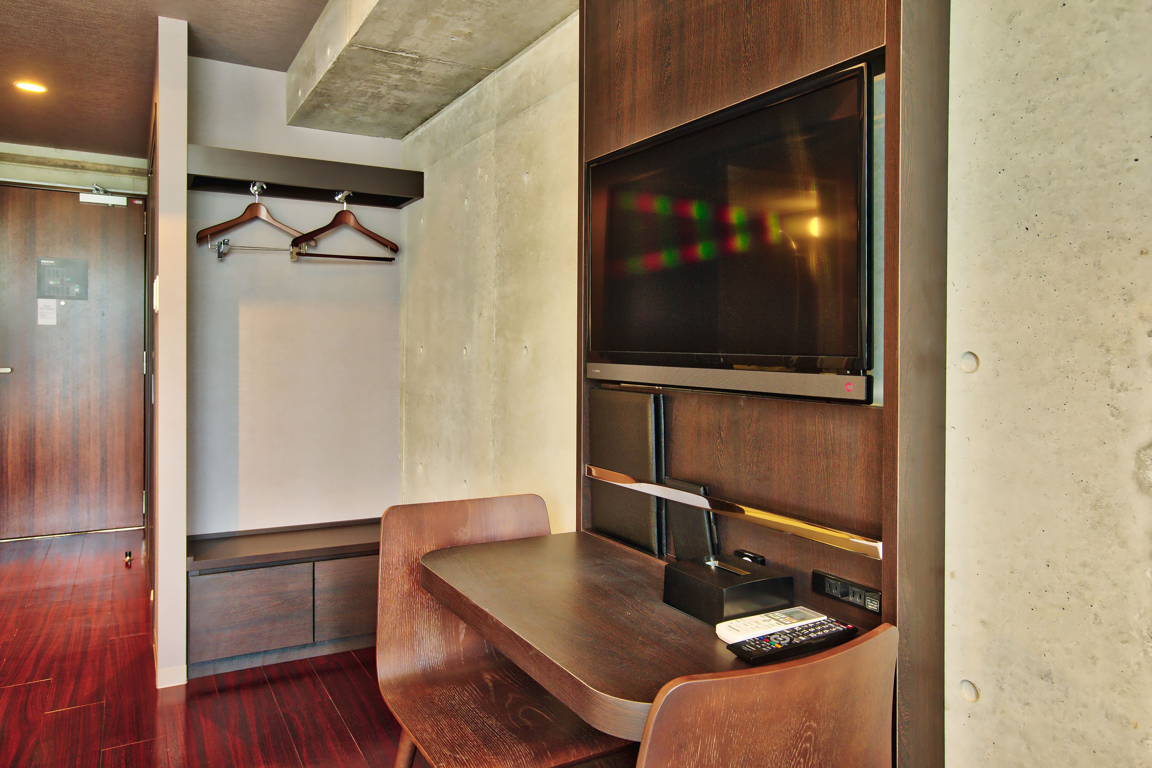 Une chambre d’hôtel moderne équipée d’un bureau en bois, d’un téléviseur à écran plat et d’un porte-manteau.