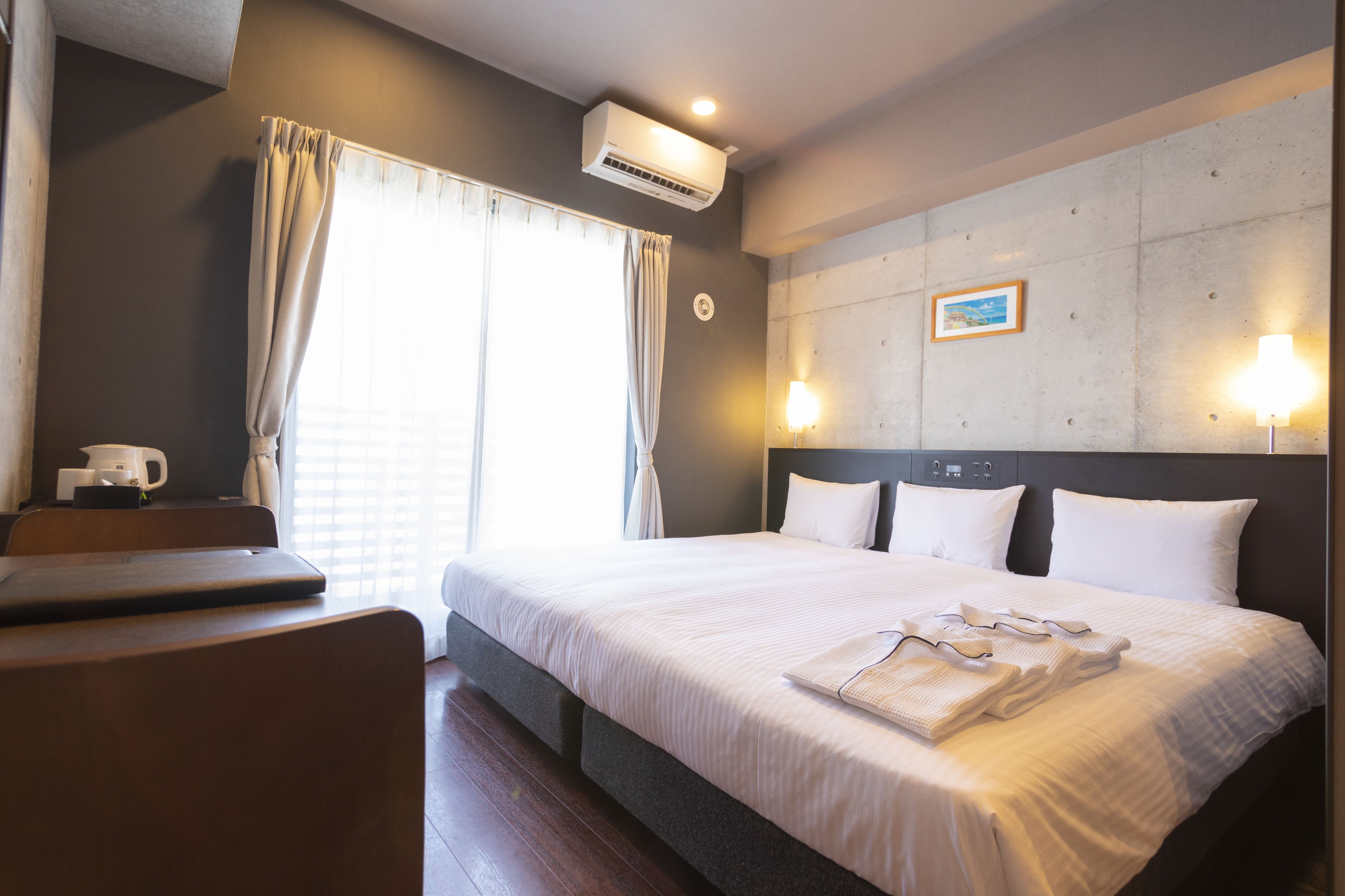 Habitación de hotel con cama, lámparas de noche, cafetera y ventana con cortinas.