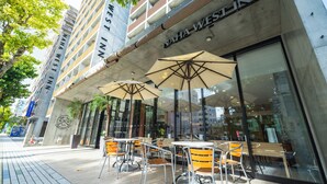 Un área de estar al aire libre con mesas y sillas, sombrillas y un edificio con un letrero que dice "NAHA WEST INN".
