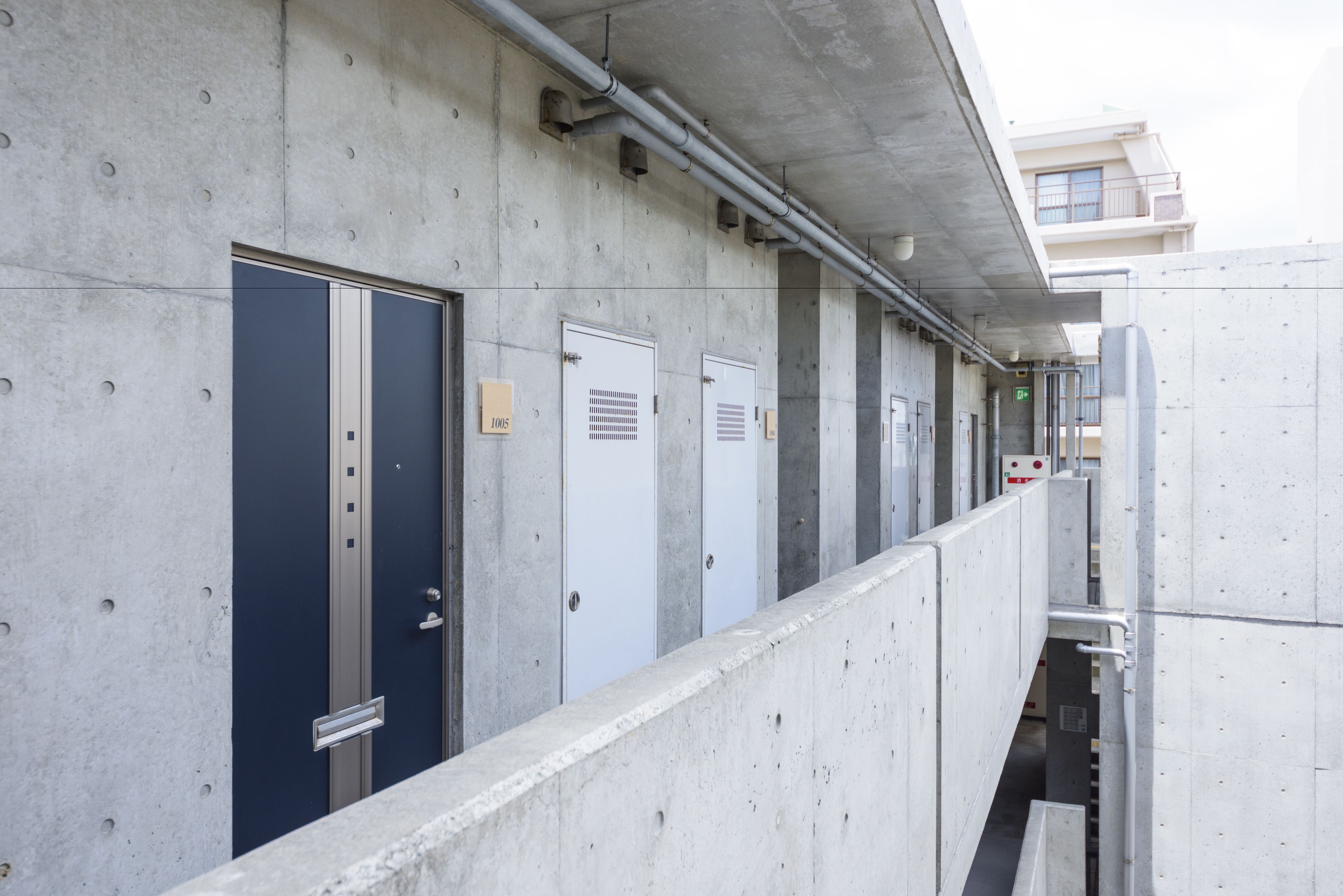 A row of concrete utility doors with metal handles and a metal railing in the foreground.