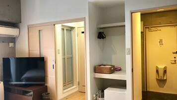 Una camera d'hotel con schermo piatto, un armadio, una porta con ripiano per scarpe e un piccolo frigorifero.