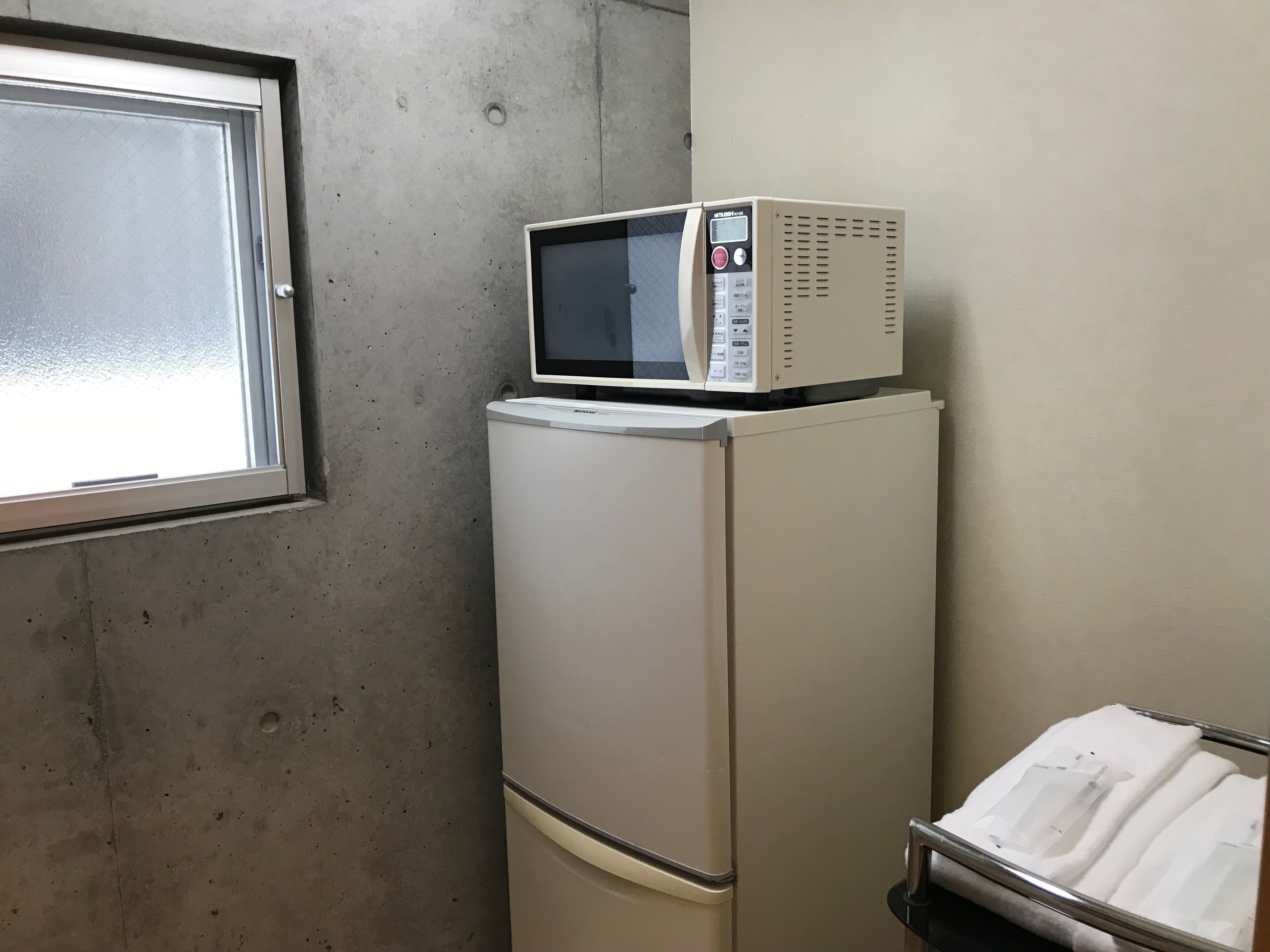 A compact kitchenette with a refrigerator, a microwave, and a small metal rack with towels.