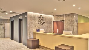 Un área de recepción con diseño moderno, que incluye un mostrador de recepción, un logotipo y tres ascensores.