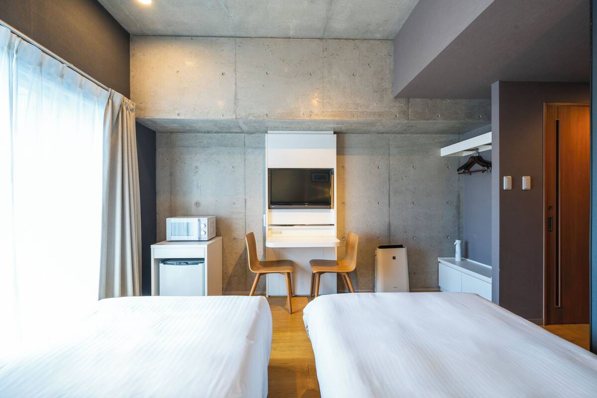 A modern hotel room with two beds, a desk, a chair, a microwave, and a wardrobe.