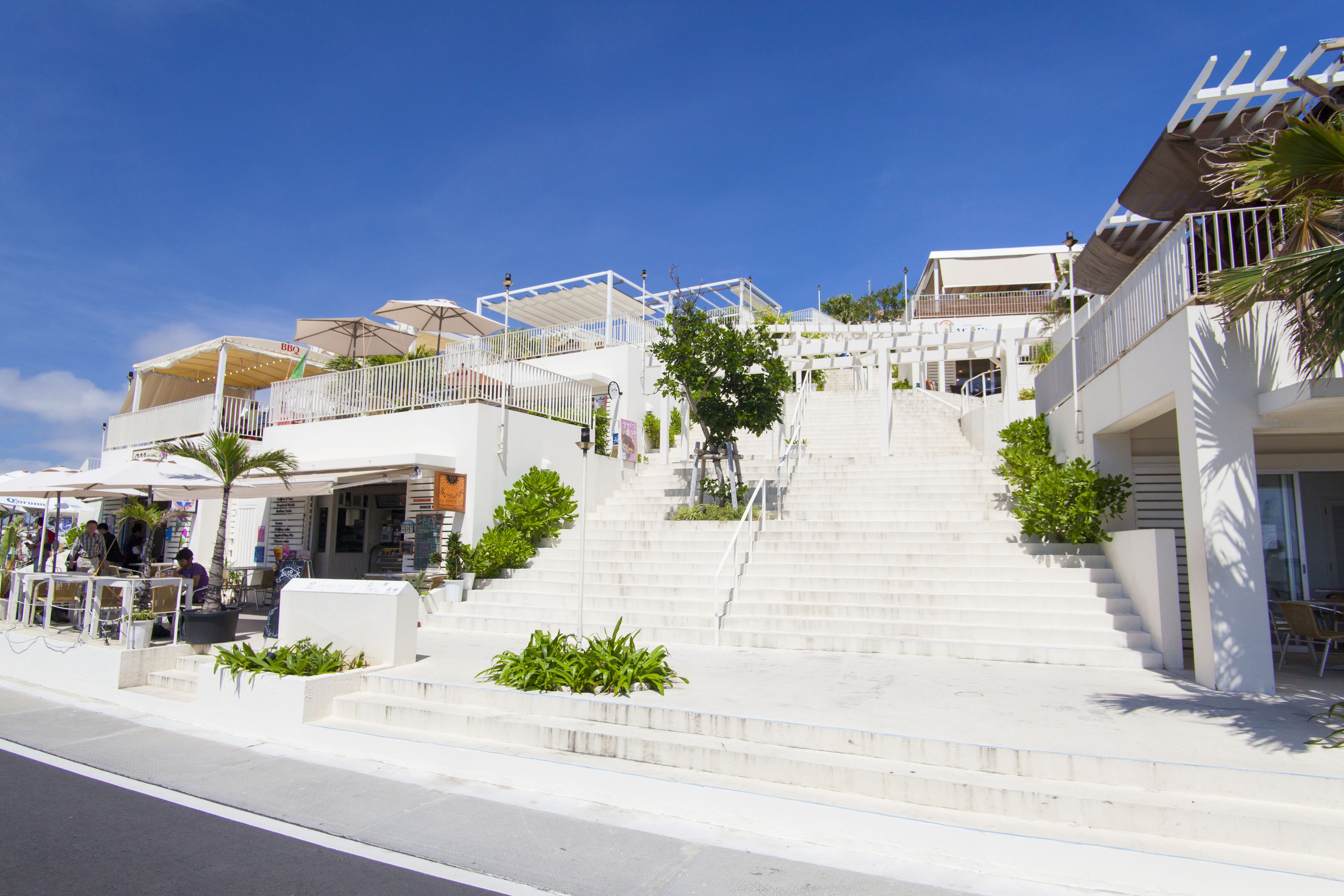 A staircase leading to a white building with outdoor seating and umbrellas.