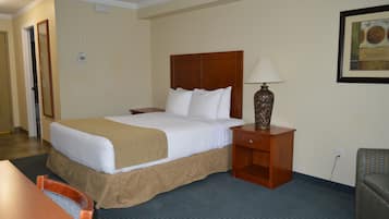 A hotel room with a large bed, a wooden nightstand with a lamp, a chair, and a small table.