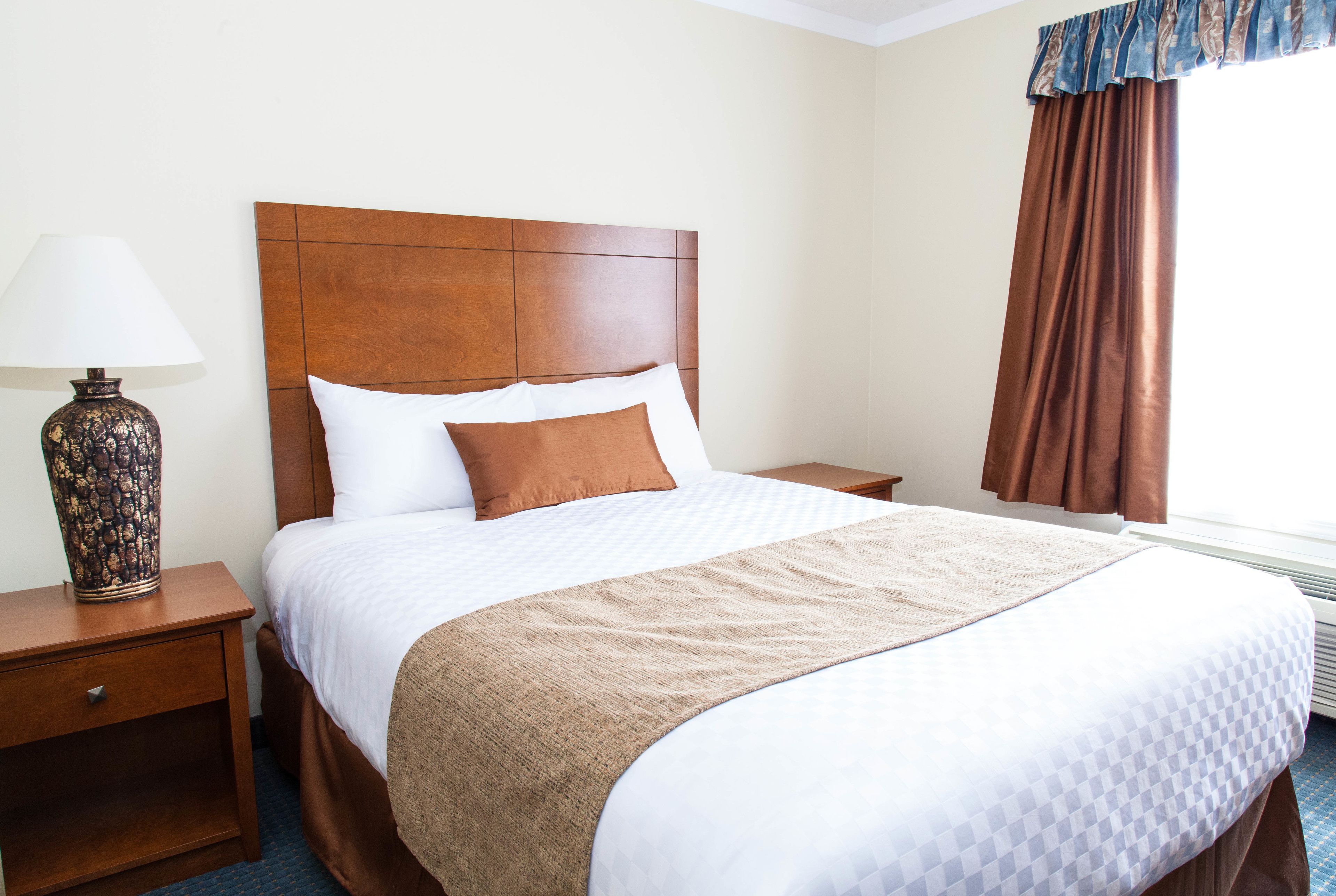 A neatly made bed with a wooden headboard, a bedside lamp, and a window with curtains.