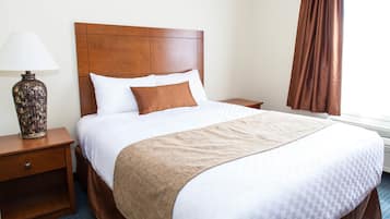A neatly made bed with a wooden headboard, a bedside lamp, and a window with curtains.