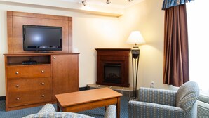 Quarto de hotel com um armário de madeira, televisão, lareira, abajur e duas poltronas estampadas.