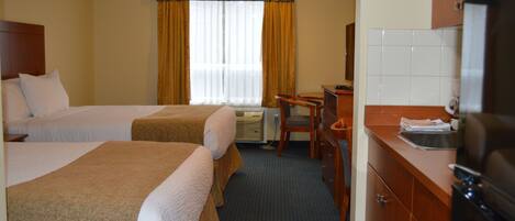 Una habitación de hotel con dos camas, un escritorio, una silla, un lavabo y un refrigerador.