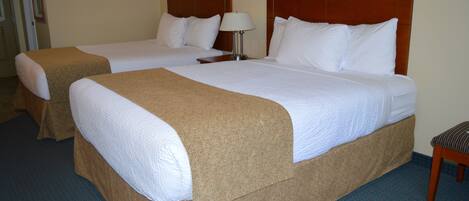 A hotel room with two beds, each with a wooden headboard, a bedside table with a lamp, and a bench by the window.